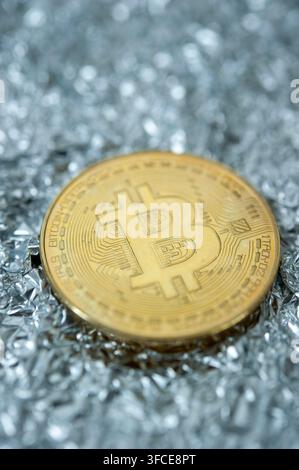 Gold-Bitcoin-Token, das auf zerknitterter Silberfolie ruht, repräsentiert Kryptowährung, digitale Finanzen und Blockchain. Stockfoto