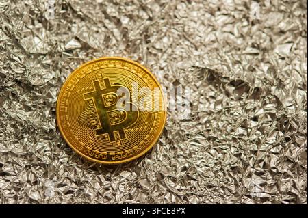 Gold-Bitcoin-Token, das auf zerknitterter Silberfolie ruht, repräsentiert Kryptowährung, digitale Finanzen und Blockchain. Stockfoto