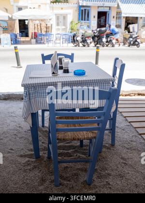 Blaue Holzstühle und Tische, die vor einem Strandcafé angeordnet sind, mit dem Meer im Hintergrund an einem hellen Küchentag Stockfoto