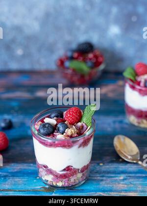 Nahaufnahme eines individuellen geschichteten Mascarpone-Desserts, das mit frischen Beeren und Minze belegt ist, wobei knusprige Granola zwischen der cremigen und fruchtigen Schicht sichtbar ist Stockfoto