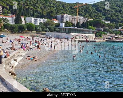 Ein lebhafter Kieselstrand in Dubrovnik im Sommer, an dem sich vielfältige Touristen an der Adriaküste sonnen und entspannen. Stockfoto