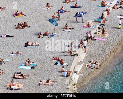 Ein lebhafter Kieselstrand in Dubrovnik im Sommer, an dem sich vielfältige Touristen an der Adriaküste sonnen und entspannen. Stockfoto