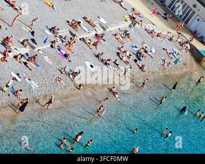 Ein lebhafter Kieselstrand in Dubrovnik im Sommer, an dem sich vielfältige Touristen an der Adriaküste sonnen und entspannen. Stockfoto