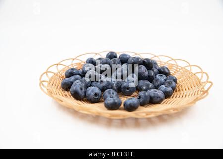 Frische reife Blaubeeren, die in einem geflochtenen Weidenkorb auf weißer Oberfläche angeordnet sind Stockfoto