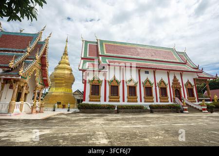 Dok kham tai, Phayao, Thailand - 27. August 2026: Wat Don Lek, goldener Chedi neben der Tempelhalle mit gestuftem rot-grünem Dach Stockfoto