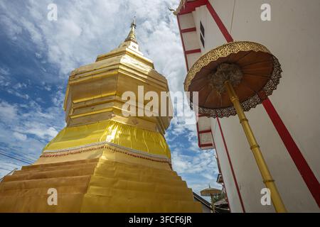 Dok kham tai, Phayao, Thailand - 27. August 2026: Wat Don Lek, goldener Chedi und zeremonielles Dach über rotgerahmter Tempelanlage Stockfoto