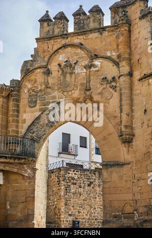 Historisches Steintor mit spitzem Bogen, geschnitzten Wappenschildern und zinnenbekröntem Brüstungsmauerwerk in der Altstadt von Baeza, Spanien. Stockfoto