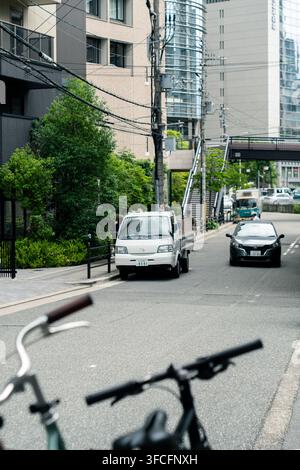 Fahrradlenker zeigen auf eine ruhige Stadtstraße mit einem kleinen Mazda-Truck und modernen Gebäuden in Osaka, Japan. 31. Mai 2025. Stockfoto