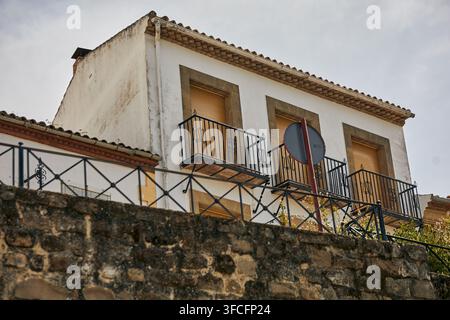 Weiß getünchtes traditionelles Gebäude mit schmiedeeisernen Balkonen, geschlossenen Läden und steinernen Fensterrahmen über einer alten Steinmauer in Baeza, Spanien. Stockfoto