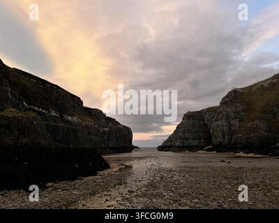 Turmhafte Felsschluchten rahmen eine Öffnung zum Meer unter pastellfarbenen Abendwolken nahe der Smoo-Höhle in Durness in den schottischen Highlands. Stockfoto