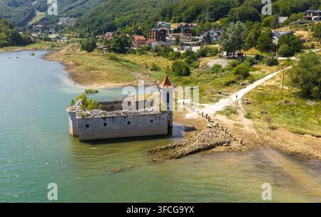 Luftbild der versunkenen Kirche St. Nikolaus im Mavrovo-See mit grünen Hügeln und Häusern im Hintergrund in Mavrovo, Gemeinde Mavro, Nord Stockfoto