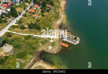 Luftbild der versunkenen Kirche St. Nikolaus, teilweise im Mavrovo-See versunken, umgeben von grünen Hügeln und ländlicher Landschaft in Mavrovo, Munici Stockfoto