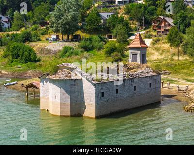 Luftaufnahme der versunkenen Kirche St. Nikolaus, teilweise im Mavrovo-See versunken, umgeben von üppigen grünen Hügeln und Bäumen in Mavrovo, Gemeinde Stockfoto