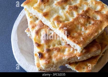 Makro-Nahaufnahme von goldenen Focaccia-Scheiben mit blasiger, gerösteter Kruste, luftiger Krume und Meersalz-Kristallen auf einem rustikalen Holzbrett Stockfoto