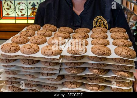 Ein Bäcker aus der Konditorei Maison des Sœurs Macarons präsentiert einen Stapel frisch gebackener Macarons de Nancy auf der Rue Saint-Dizier in Nancy, Grand Est, Frankreich. Die traditionellen Mandelmakronen unterscheiden sich von den bekannteren französischen Macaron-Sandwichkeksen durch ihre gerissene, ungefüllte Kruste. Der Tradition nach suchten Nonnen während der Französischen Revolution Zuflucht im Haus der Konditorei und backten dort die ersten Macarons – historisch nicht zweifelsfrei bestätigt, aber der Ursprung des Namens „Sœurs Macarons“.  Stockfoto