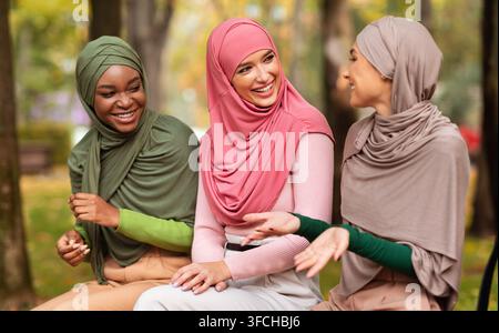 Drei Arabische Damen In Hijab Sprechen Auf Der Bank Im Stadtpark Sitzen Und Unterhaltung Genießen. Wochenendausflug, Muslimische Damen Treffen Sich Mit Freunden. Stockfoto
