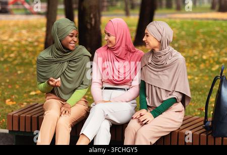 Drei Muslimische Damen Im Hijab-Kopftuch Sprechen Auf Der Bank Im Park Draußen. Weibliche Freundschaft, fröhliche islamische Studenten genießen Unterhaltung C Stockfoto