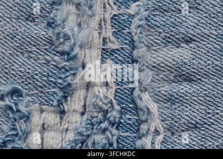 Extremer Makroaufnahm von zerrissenem Denimstoff, der ausgefranste Fäden und die gewebte Baumwolltextur zeigt Stockfoto