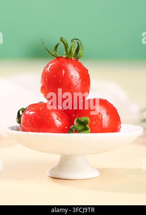 Drei nasse rote Tomaten, die auf einem weißen Teller gestapelt sind, vor einem grünen Hintergrund. Stockfoto