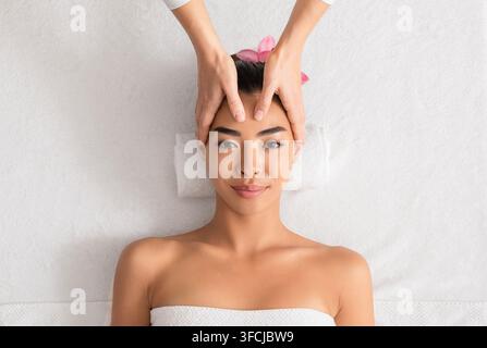 Junge asiatische Frau genießt Anti-Aging-Gesichtsmassage im Spa-Salon. Masseurin-Therapeutin, die Kopf- und Gesichts-Schönheitsbehandlungen zu entspannter koreanischer La macht Stockfoto