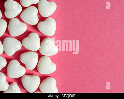 Gereichte weiße herzförmige Bonbons auf einem rosafarbenen Papierhintergrund, die eine süße, romantische Komposition mit reichlich Platz für Valentinskarten, Werbung Stockfoto