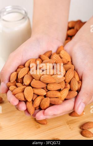 Hände halten einen Haufen Mandeln auf einer Holzoberfläche mit Milch im Hintergrund. Stockfoto