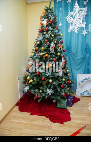 Ein wunderschön geschmückter Weihnachtsbaum steht unter einem luxuriösen Kronleuchter, umgeben von farbenfrohen Geschenktüten in einem klassischen Raum. Er schafft eine warme und fe Stockfoto