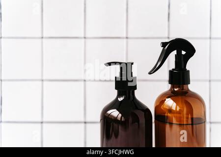 Zwei bernsteinfarbene Glassprühflaschen mit schwarzen Sprühauslösern auf einem sauberen weißen Fliesenhintergrund. Minimale Komposition mit Kopierraum für Reinigung, Kosmetik Stockfoto