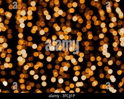 Abstrakte goldene Bokeh-Lichter, die vor einem dunklen Hintergrund leuchten. Warme, unscharf ausgeleuchtete Beleuchtung schafft eine festliche und elegante Atmosphäre, ideal für Christ Stockfoto