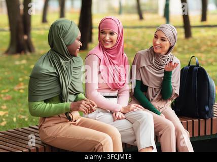 Drei Verschiedene Muslimische Damen In Hijab Unterhalten Sich Bei Gesprächen Und Herbsttag Auf Der Bank Im Stadtpark. Moderne Islamische Studentinnen Spendi Stockfoto