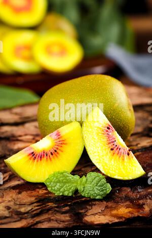 Geschnittener goldener Kiwifrucht auf rustikalem Holz mit ganzer Frucht im Hintergrund. Stockfoto