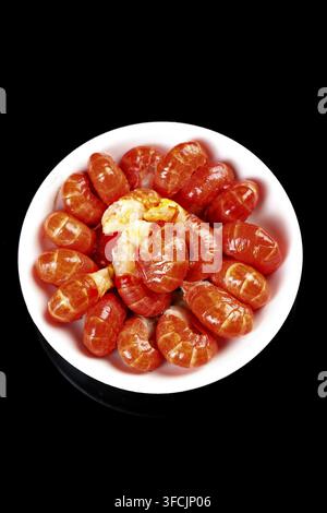 Teller mit geschälten Mandarinen, die auf einem schwarzen Hintergrund arrangiert sind. Stockfoto