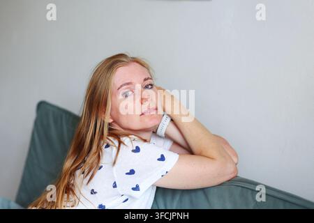 Junge Frau, die ihr Haupt hält, während sie zu Hause ruht, Konzept von Kopfschmerz, Burnout, Müdigkeit, Stress und Bedürfnis nach Ruhe. Stockfoto