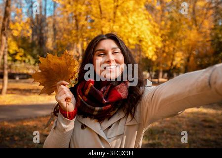 Schöne junge Frau in modischen Herbst Kleidung mit Strauß Herbstlaub und Selfie im Park Stockfoto