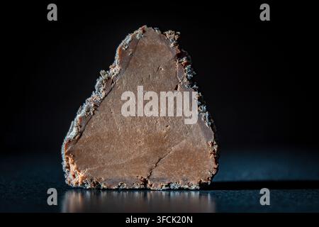 Nahaufnahme-Makroaufnahme von Schokoladen-Trüffelbonbon, der in der Hälfte geschnitten ist und seine glatte, reiche Ganache-Füllung zeigt, isoliert auf dunklem, stimmungsvollen Hintergrund Stockfoto