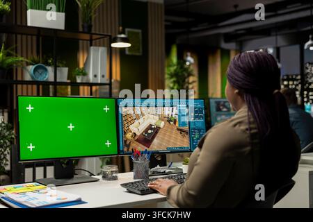 Schwarze Grafikdesignerin verwendet ein isoliertes Mockup und CAD-Software, um einen modernen Grundriss zu erstellen, ein 3D-Modellierungsprogramm und Chroma-Key auf einem Dual-Monitor Stockfoto