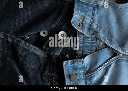 Nahaufnahme, die kontrastierende dunkle und helle Denimtexturen mit Metallknöpfen und einem Reißverschluss zeigt Stockfoto