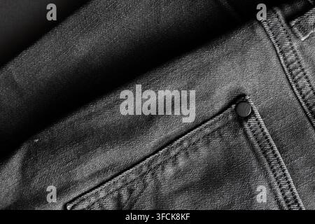 Schwarzer Denimjeansstoff zeigt eine strukturierte Oberfläche mit Tasche und Niete Stockfoto