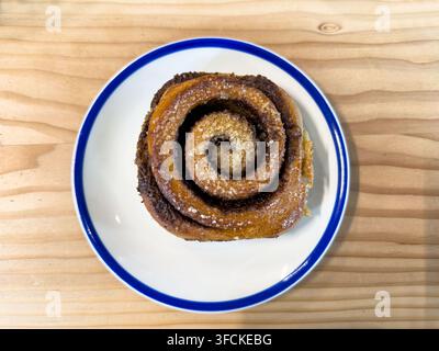 Oberansicht Flachlayout von Zimtschnecke auf weißem Teller mit blauem Rand, fotografiert auf Holztisch Stockfoto