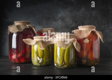 Konserven fermentierten Früchte und Gemüse, Pflaume, Gurke, Tomate, die in Gläsern auf dunklen Holz- Board. Verschiedene Arten von Fermentiert. Horizontale Ausrichtung. Stockfoto