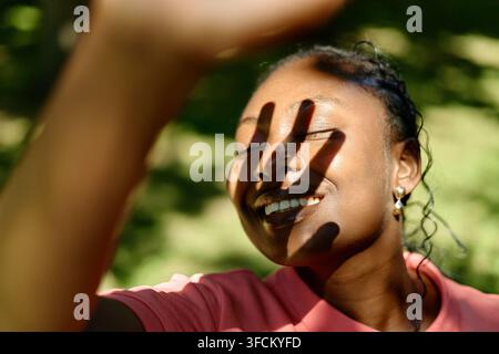 Lächelnde schwarze Frau, die ihre Augen während der Outdoor-Therapie vor der Sonne schützt Stockfoto