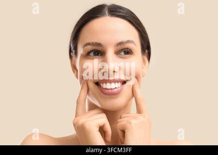 Hautpflege- und Schönheitsroutine, junge Frau mit gesunder, strahlender Haut, die lächelt und Wangen auf einem neutralen beigen Hintergrund für Kosmetikwerbung berührt Stockfoto