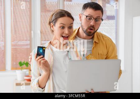 Online-Shopping-Rabatt und Verbrauchereinsparungen, aufgeregtes Paar verwendet Kreditkarte und Laptop für E-Commerce-Angebote zu Hause mit Überraschung und Freude Stockfoto