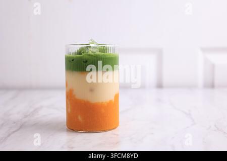 Eisgekühlter Mango-Matcha-Latte in hohem Glas auf dem weißen Tisch, Kopierraum für Text Stockfoto