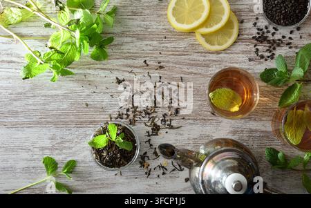 Zitronen- und Minztee frisch gebraut auf einer hölzernen Küchenbank mit Zutaten wie Zitronenscheiben, frischen Minzzweigen und einer Schüssel mit getrocknetem grünem Tee Stockfoto