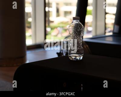 Eine klare Plastikwasserflasche, gefüllt mit erfrischendem Mineralwasser, steht auf einer dunklen Fitnessstudio-Oberfläche. Tröpfchen von Kondenswasser bedecken die Flasche, was Hitze darstellt Stockfoto