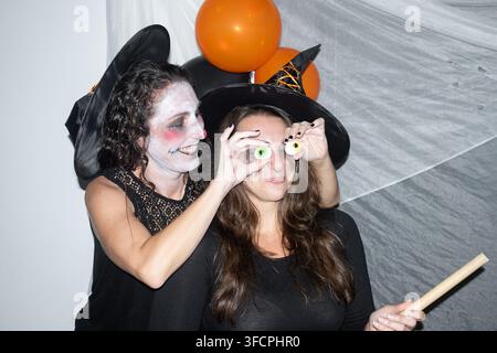 Zwei Freundinnen in Hexenkostümen haben Spaß mit Gummi-Augenbonbons während einer geschmückten Halloween-Party. Stockfoto