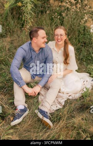 Fröhliches junges Paar lacht zusammen und sitzt auf einem Feld Stockfoto