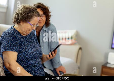 Ältere Frau lernt, wie man ein Smartphone benutzt, mit ihrer Tochter Stockfoto