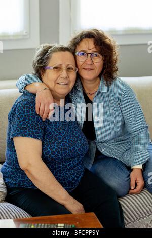 Liebende Frau umarmt ihre ältere Mutter auf einer Couch Stockfoto